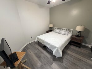 A bedroom with a bed, two bedside tables with lamps, a desk with a computer, and a ceiling fan.