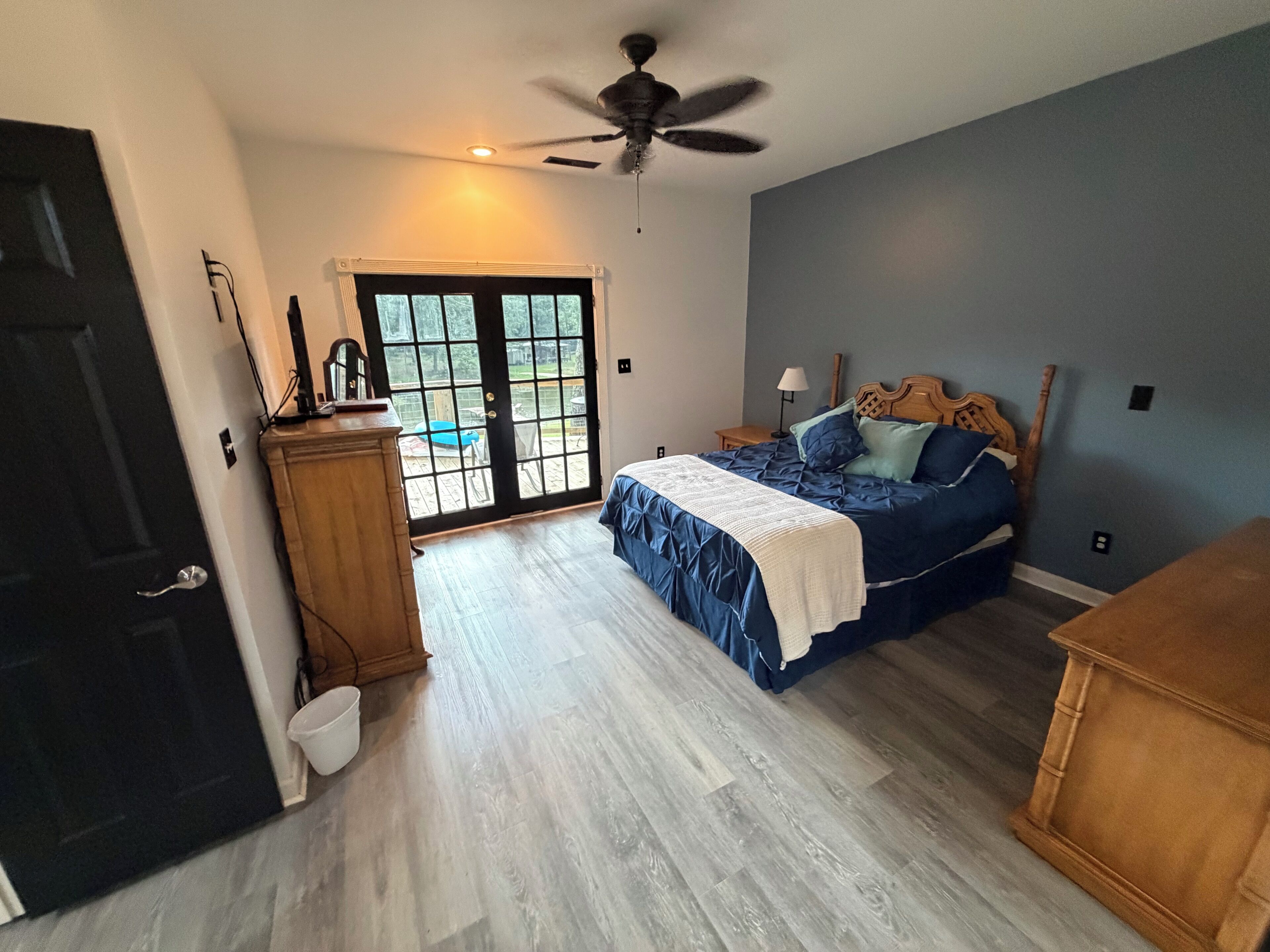 Una camera da letto con un letto, una ventola a soffitto, una porta e vista su uno spazio esterno attraverso una porta in vetro.