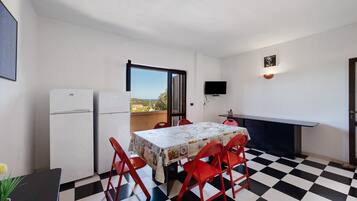Une cuisine de taille réduite comprenant une table à manger, des chaises, un réfrigérateur et un téléviseur.