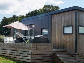 Eine moderne Holzhütte mit einer Terrasse und Gartenmöbeln, sowie einer Treppe zum Eingang.