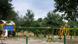 An outdoor exercise area with various fitness equipment, including spinning bikes and strength machines, surrounded by trees and a grassy area. - Mobile home with AC - 6 guests (Sainte-Reine-de-Bretagne)