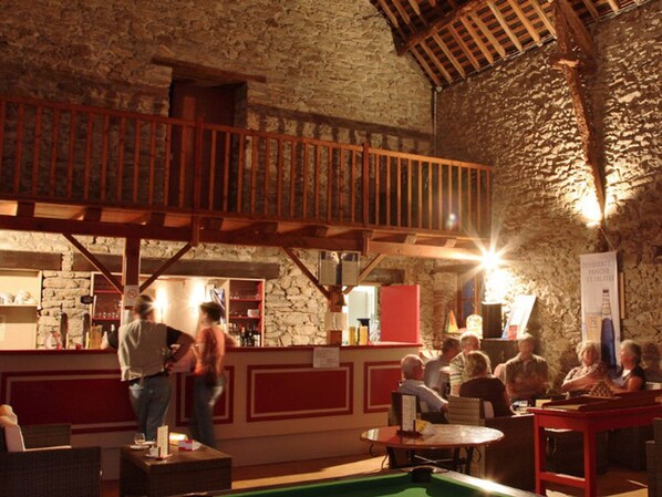 Eine rustikale Bar mit Steinwänden, Holzbalken und einem Billardtisch.