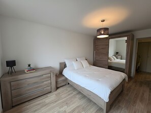 A bedroom with a bed, a dresser, a mirror, and a lamp. - Charming central apartment - 4 guests (Luxeuil-les-Bains)