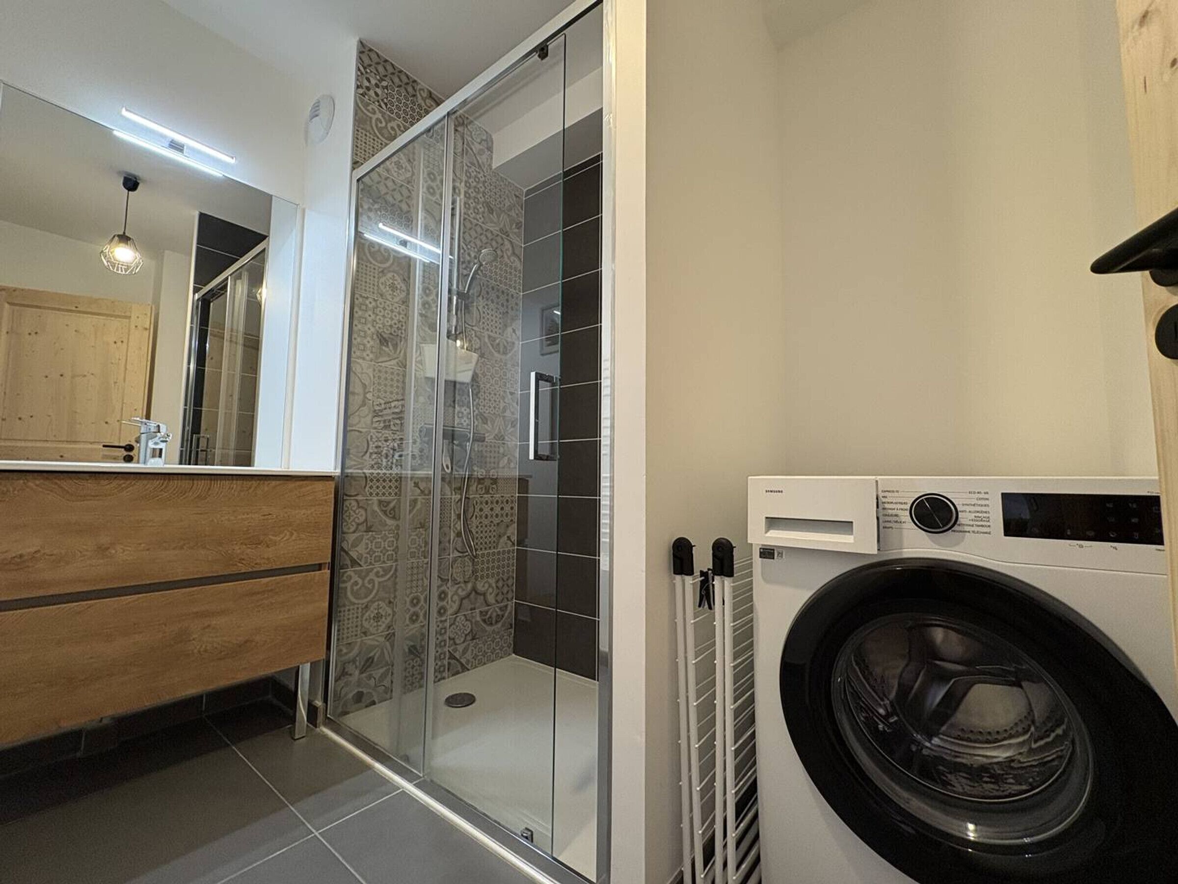 Une salle de bain moderne avec une douche à parois de verre, un meuble-lavabo en bois et un lave-linge à chargement frontal.