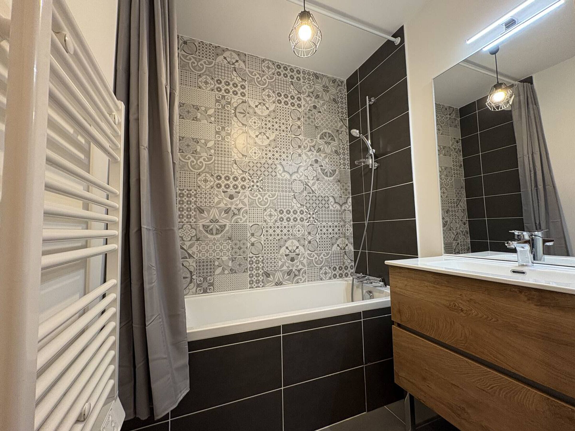A bathroom with a bathtub, a shower, a vanity with a mirror, and patterned tiles on the walls.