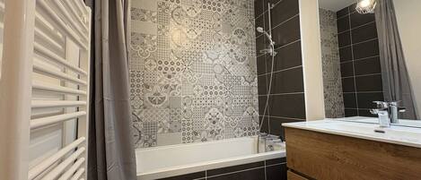 A bathroom with a bathtub, a shower, a vanity with a mirror, and patterned tiles on the walls.