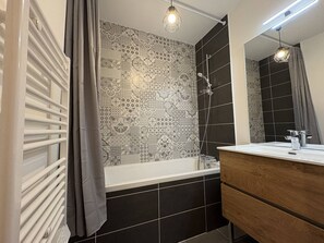A bathroom with a bathtub, a shower, a vanity with a mirror, and patterned tiles on the walls. - Modern apartment with parking - 4 guests (Valmorel)