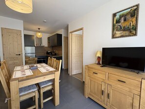 A modern kitchen with dark appliances, a dining table with chairs, and a TV on a wooden cabinet. - Modern apartment with parking - 4 guests (Valmorel)