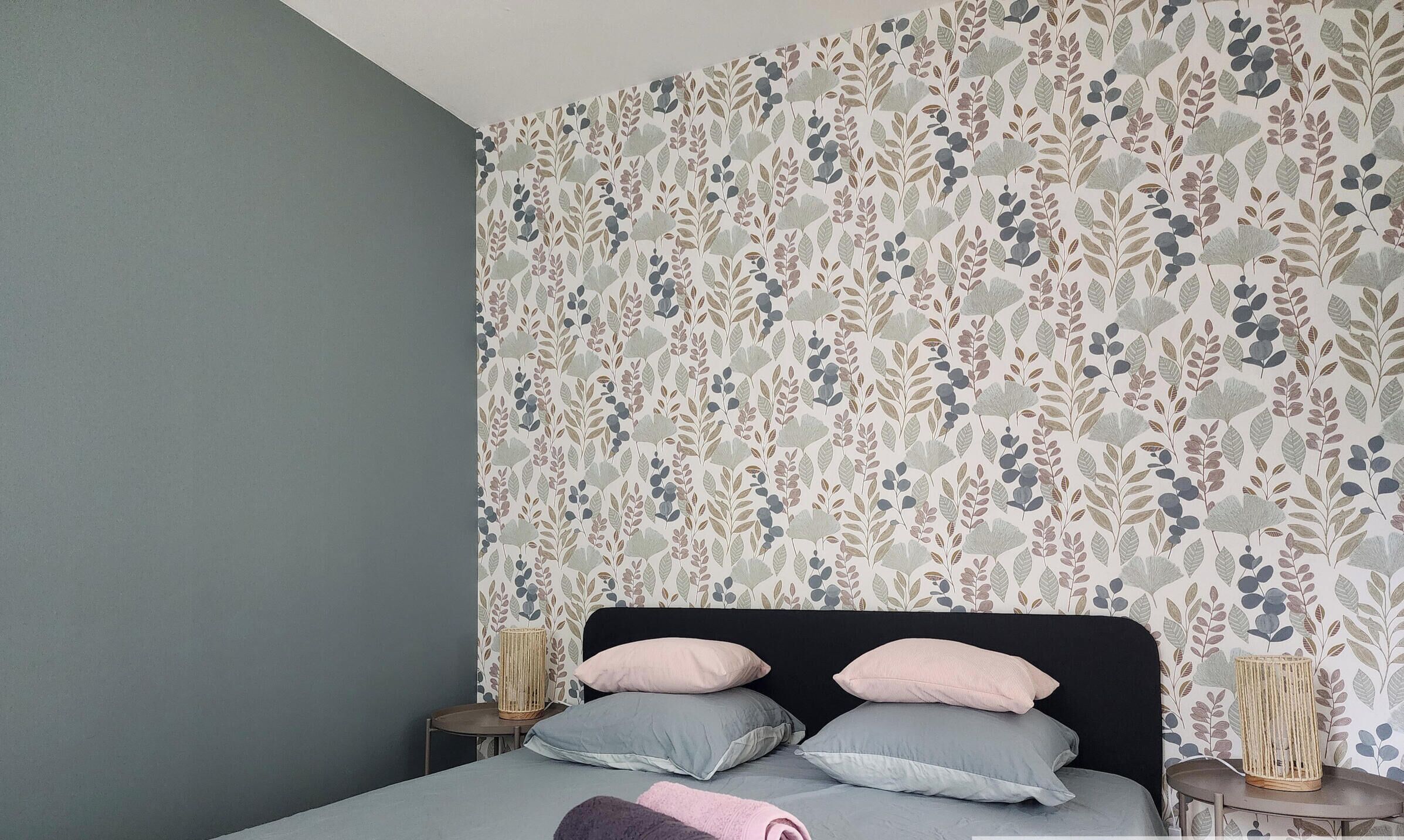 Un dormitorio con cama, almohadas, una mesita de noche y una pared con diseño de hojas.