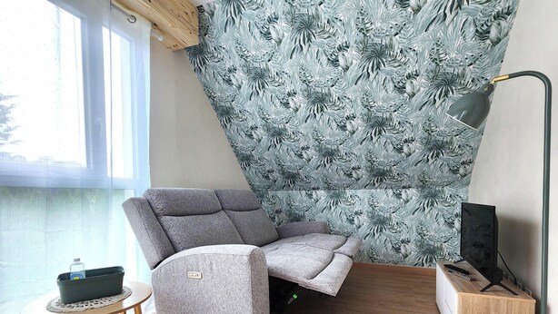 Ein Eckzimmer mit grauem Sofa, Fernseher und einem fenster mit Vorhängen.