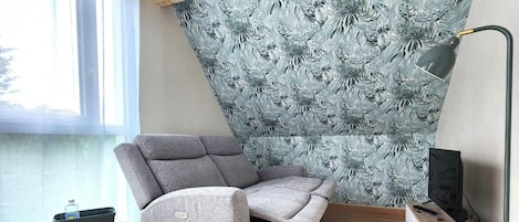 A corner room with a grey sofa, a television, and a window with curtains.