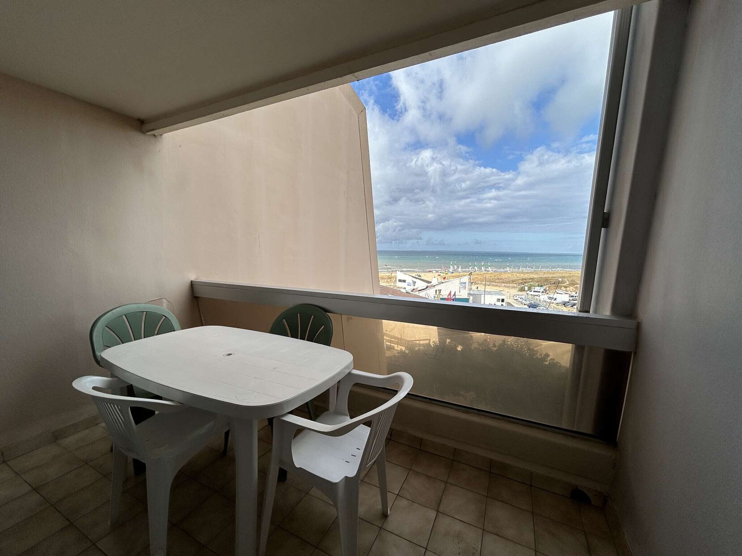 Uma varanda com vista para a praia e o oceano, uma mesa branca e duas cadeiras.