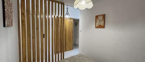 A bedroom with a bed, a wooden slat partition, a hanging light fixture, and two wall-mounted artworks.