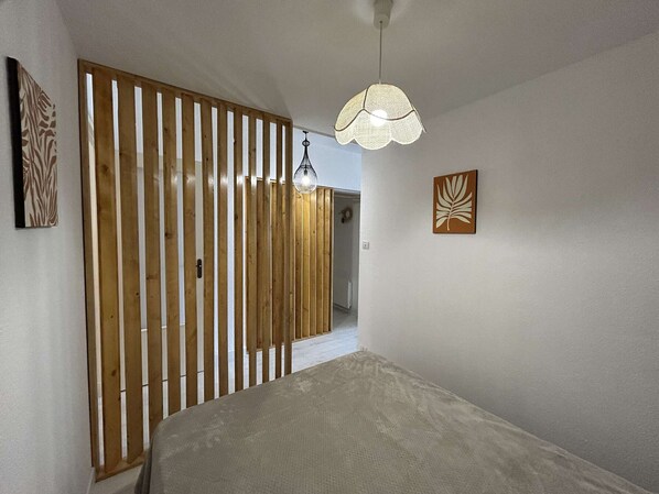 Een slaapkamer met een bed, een houten lattenwand, een hanglamp en twee kunstwerken aan de muur.
