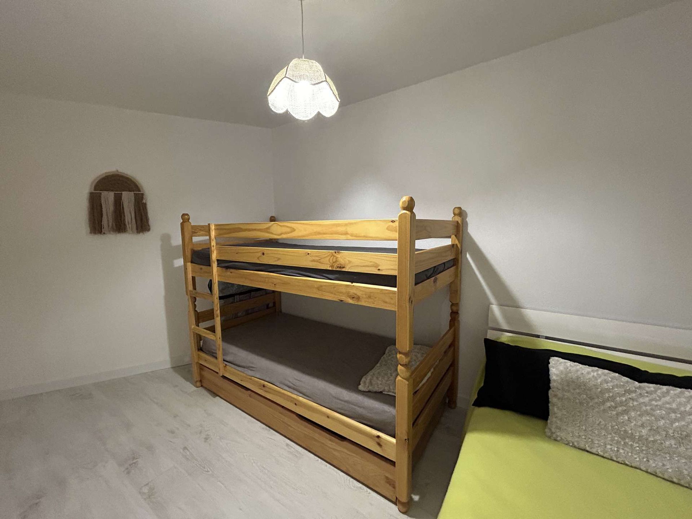 Ein Stockbett mit Holzrahmen und einer Matratze, ein kleines Fenster mit Vorhängen sowie eine Pendelleuchte.
