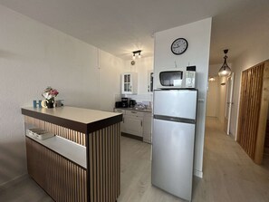 Een kleine keuken met een ingebouwde magnetron, een koelkast en een klok aan de muur.