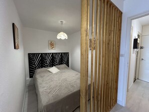 A bedroom with a bed, a headboard with a leaf pattern, a hanging light fixture, and a door leading to another room. - Apartment with sea view - 6 guests (Saint-Jean-de-Monts)