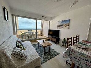 Een woonkamer met een bank, een salontafel, een televisie en een eethoek met een tafel gedekt voor twee personen.