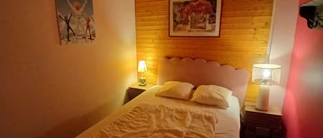 A bedroom with a wooden headboard, a bed with pillows, a nightstand with a lamp, and a wall with a framed picture.