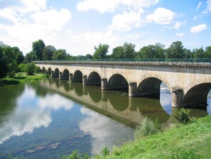 Un pont de pierre à arches multiples enjambant une rivière paisible, entouré de verdure et sous un ciel dégagé.