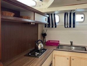 Cocina compacta con estufa a gas, lavamanos y ventana con cortinas.