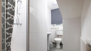A bathroom with white tiles, a shower, a toilet, and a sink. - Charmstay Swiss Cottage (London)