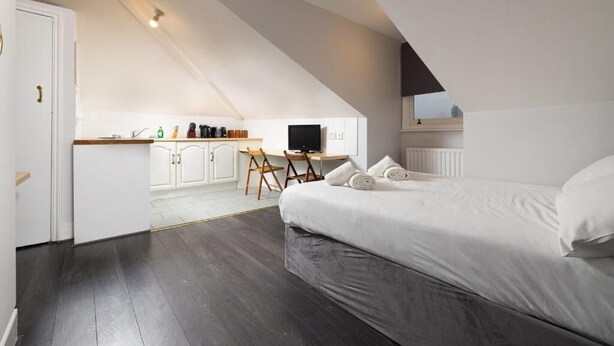 A bedroom with a large bed, a desk, and a chair in a loft-style room with a sloped ceiling. - Charmstay Swiss Cottage (London)