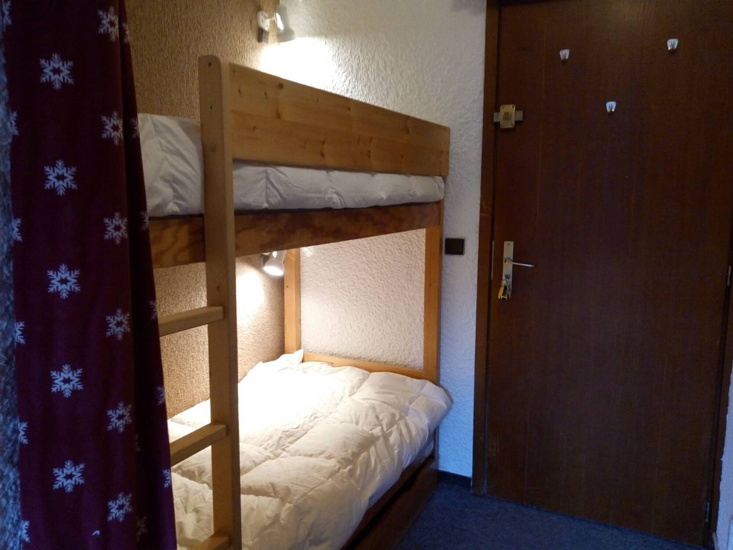 A bunk bed with a wooden frame and white bedding, a door with a handle, and a carpeted floor.