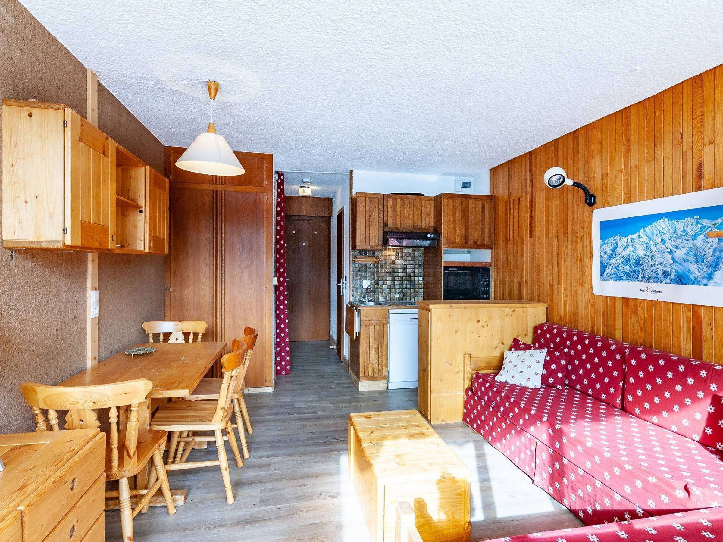 A cozy room with wooden furniture, a dining table, a sofa, and a kitchen area with cabinets and appliances.
