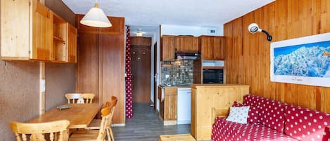 Una habitación acogedora con muebles de madera, una mesa de comedor, un sofá y una zona de cocina con armarios y electrodomésticos.