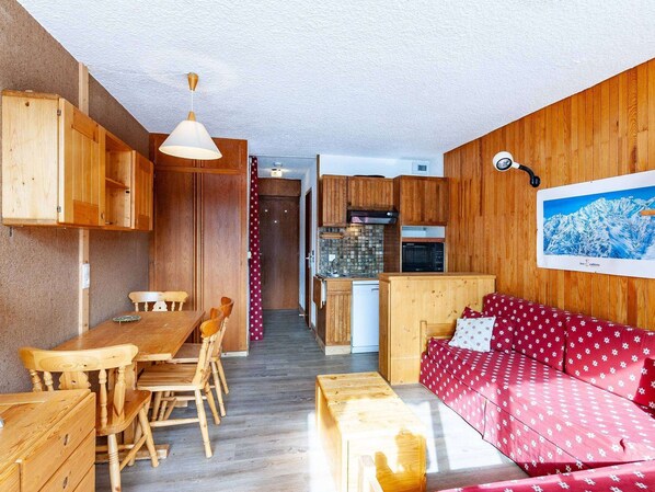 A cozy room with wooden furniture, a dining table, a sofa, and a kitchen area with cabinets and appliances.
