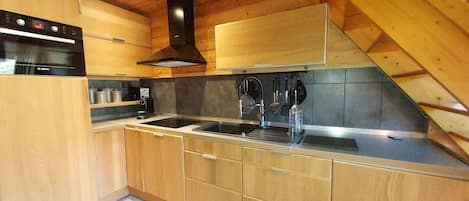 Een keuken met houten kastjes, een zwart fornuis en een roestvrijstalen spoelbak.