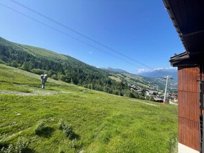 A rural landscape with a clear sky, a wooden building, and a distant village. - Cozy apartment, slope view - 6 guests (Valmorel)