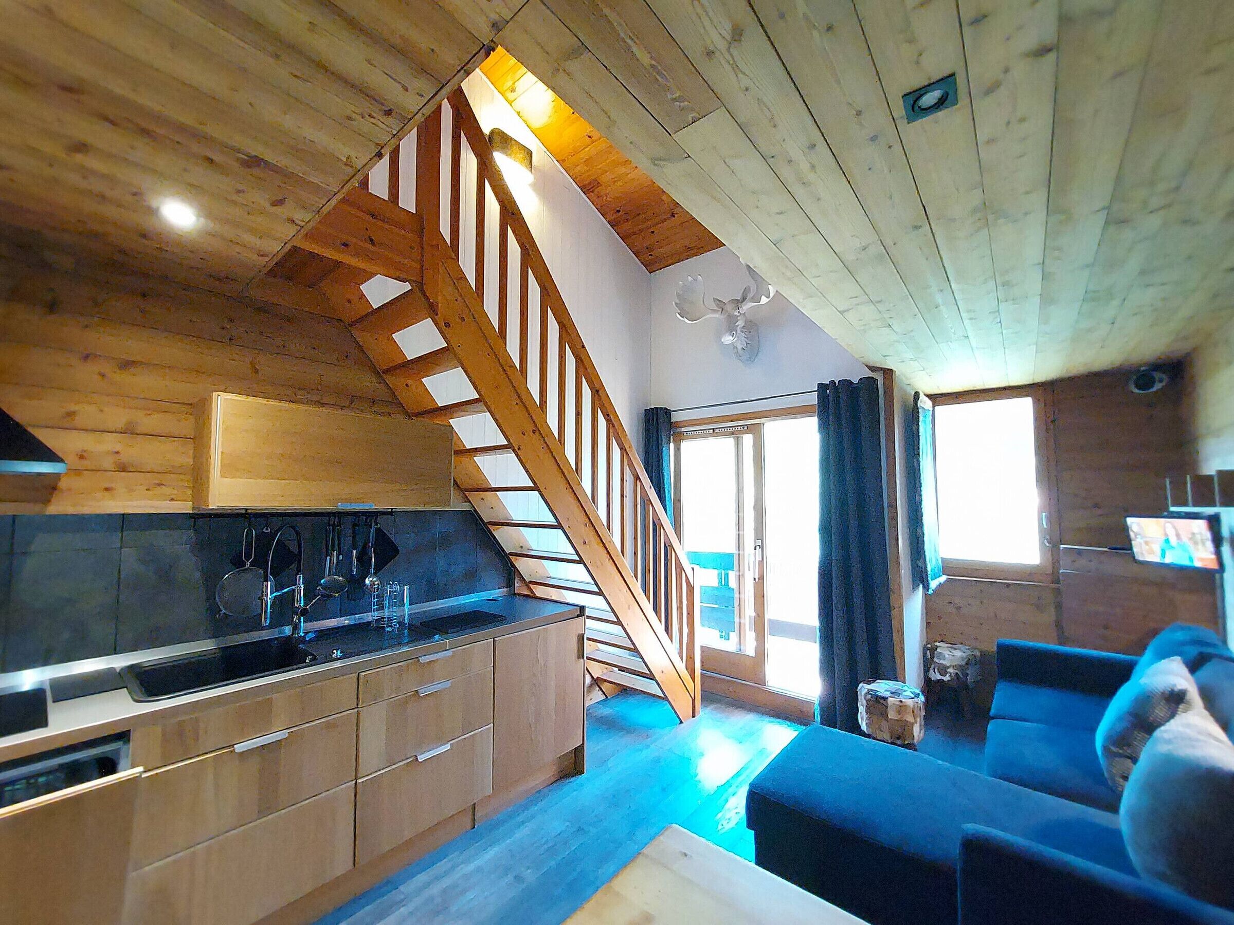 A wooden interior with a kitchen, a staircase, and a seating area.