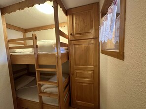 Un lit superposé avec une échelle, une porte en bois et une fenêtre avec un rideau.