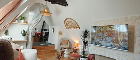 A modern living room with a sloped ceiling, a large painting, and a cozy seating area with a teddy bear.
