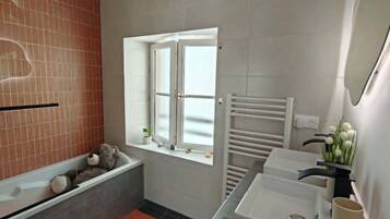 Un baño moderno con bañera, ventana, lavamanos y espejo.