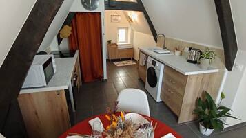 Un comedor con una mesa roja dispuesta para seis, una cocina con lavadora y un altillo con vigas a la vista.