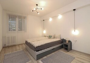 Een slaapkamer met een bed, nachtkastjes, een hanglamp en een raam met gordijnen.
