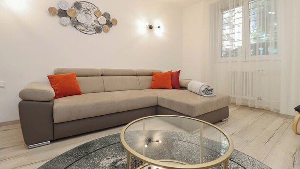 Una sala de estar moderna con un sofá seccional color beige, una mesa de centro de vidrio y un adorno de pared.