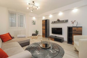A modern living room with a sofa, a coffee table, a TV, and a decorative plant. - Comfortable 1 -  Bedroom Apartment by the Danube (Budapest)