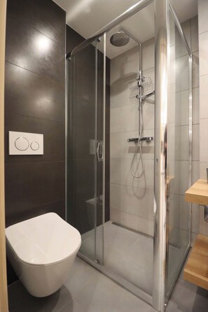 Un baño moderno con ducha de vidrio, inodoro y tocador de madera.