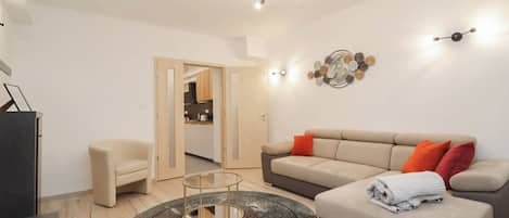 A modern living room with a sofa, armchair, coffee table, and a dining area visible through an open door.