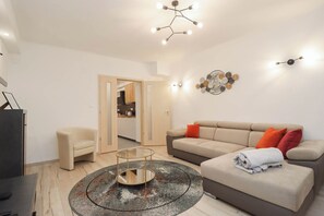 Ein modernes Wohnzimmer mit Sofa, Sessel, Couchtisch und einem Essbereich, der durch eine offene Tür sichtbar ist.