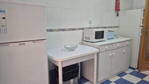 A compact kitchen with a white refrigerator, a microwave, and a small table with a glass bowl. - Apartment 'Rocha Waves' with Balcony, Wi-Fi and Air Conditioning (Portimão)