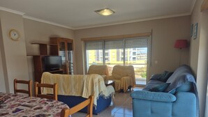 A living room with a sofa, chairs, a TV, and a view through the window. - Apartment 'Rocha Waves' with Balcony, Wi-Fi and Air Conditioning (Portimão)