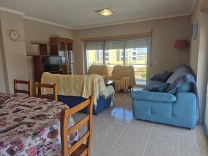 Ein Wohnzimmer mit einer Couch, Sesseln, einem Fernseher und Blick aus dem Fenster.