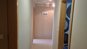 A hallway with a carpeted floor, a framed picture on the wall, and a door leading to a room with a blue tiled floor. - Apartment 'Rocha Waves' with Balcony, Wi-Fi and Air Conditioning (Portimão)