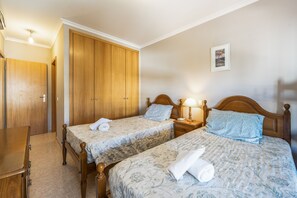 A hotel room with two single beds, a wooden wardrobe, a bedside table with a lamp, and a framed picture on the wall. - Apartment 'Rocha Waves' with Balcony, Wi-Fi and Air Conditioning (Portimão)