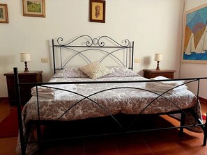 Ein Bett mit Metallgestell, zwei Nachttische mit Lampen und ein Bild an der Wand.